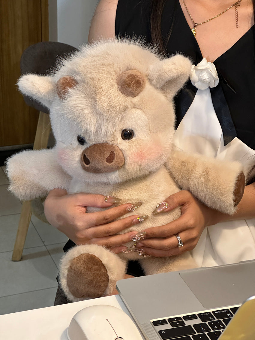 Biscuit cream Highland cow plushie held beside a laptop, showing its real size.